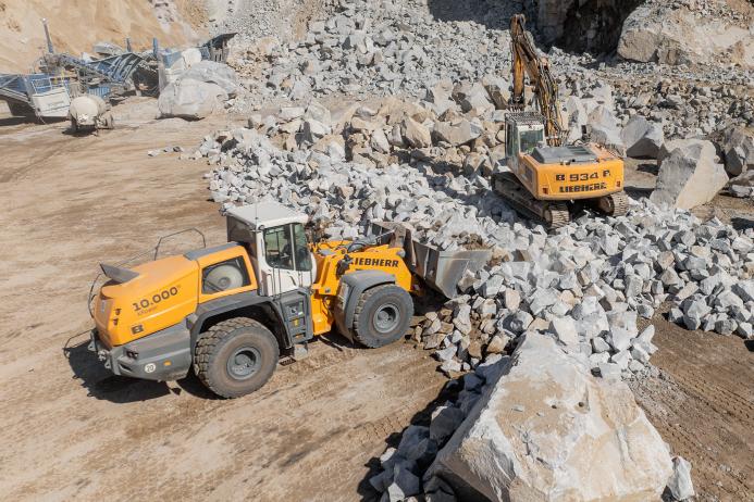 Teamwork in action: a Liebherr crawler excavator breaks large rocks, while the anniversary machine transports the material