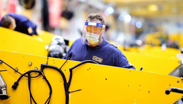 JCB shop-floor workers returning to work are being provided with masks and visors JCB worker woith visor